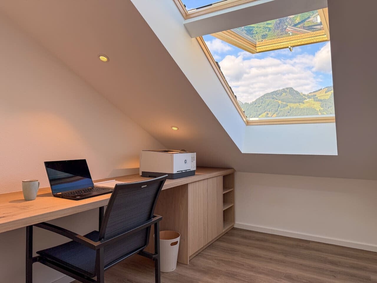 A modern room with a skylight, a desk with a laptop, and a printer.
