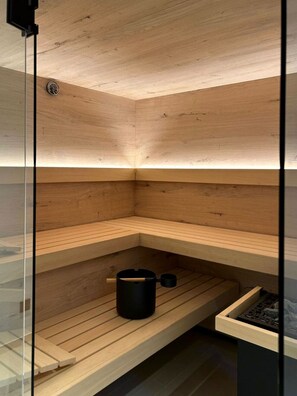 A sauna with wooden benches and a black container on the lower shelf. - ACHZEIT | Moden Alpine Home | Sauna, Fireplace & Garden near Oberstdorf | 3 BR (Fischen)