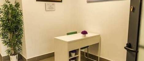 A small, clean room with a white desk, a potted plant, and a framed picture on the wall.