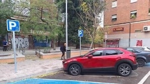 A red car parked in a disabled parking space with a blue handicap parking sign. - Isabel Guest House Room 2 (Madrid)