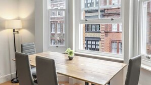 Un salón de conferencias con una mesa de madera, cuatro sillas, una lámpara y una ventana con vistas a edificios.