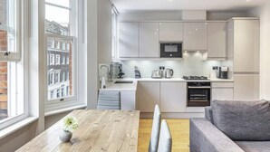 Una cocina moderna con armarios blancos, microondas integrado y un comedor con mesa de madera y sofá gris.