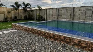 A rectangular swimming pool with a stone border, surrounded by a concrete wall and a gravel area. - SC RESORT (Concepcion)
