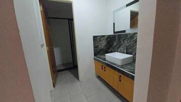 Un baño con lavamanos blanco, encimera de mármol y espejo encima. Se ve una puerta que da a otra habitación.