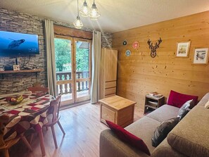 A cozy living room with a wooden wall, a television, a dining table with chairs, and a sofa. - Studio cabin 4 pers, balcony, Valloire (Valloire)