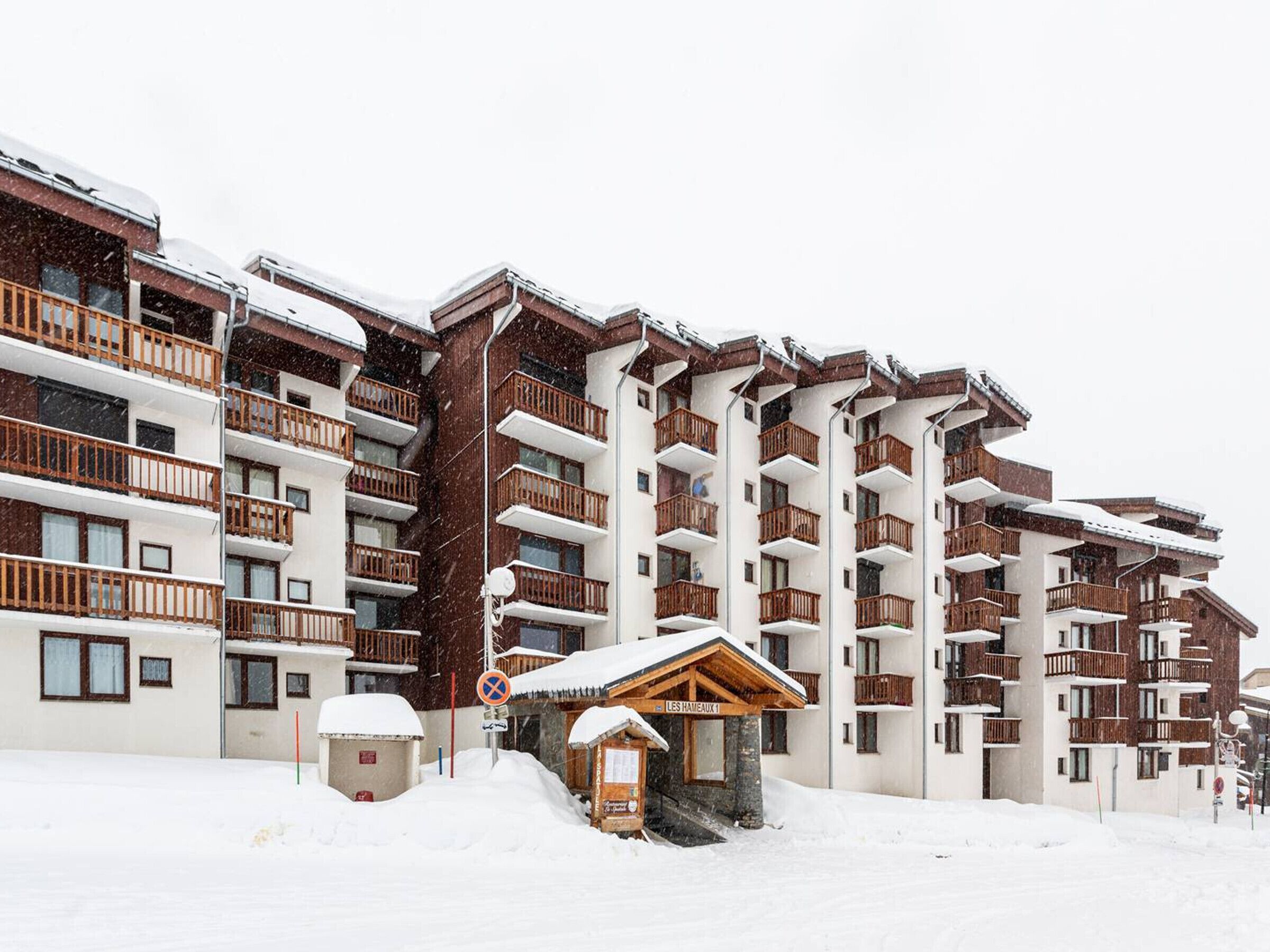 Un hotel de varios pisos con balcones, un telesilla y un pequeño edificio de madera con la inscripción 'LES HAMEAUX 1'.