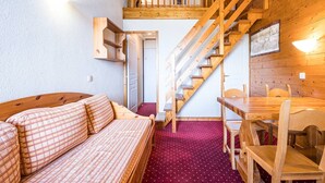 A cozy room with a wooden staircase, a bed with plaid bedding, a dining table with chairs, and a small wooden shelf. - Charming apartment for 4 with mezzanine, near slopes in Plagne Villages (Plagne Villages)