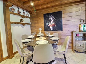 A dining area with a wooden table set for four, chairs, and a decorative wall with a framed picture.