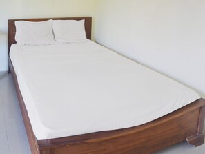 A single bed with a wooden frame and white bedding in a room with plain walls and a tiled floor.