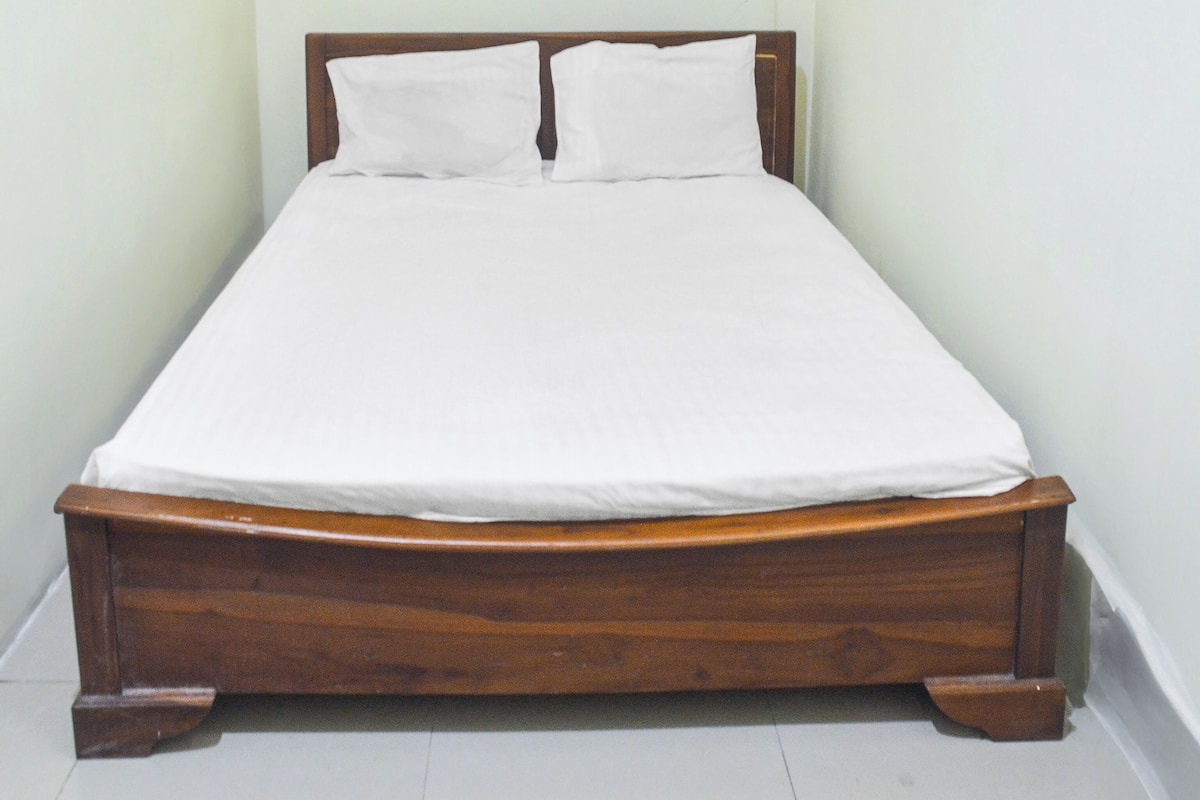 Ein Einzelbett mit Holzrahmen und weißer Bettwäsche in einem Raum mit schlichten Wänden und weißem Bodenbelag.