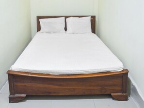 A single bed with a wooden frame and white bedding in a room with plain walls and white flooring.