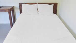 A single bed with a wooden headboard and white bedding in a room with plain walls.