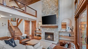 A spacious living area with a stone fireplace, leather sofas, and a large flat-screen TV mounted above the fireplace.