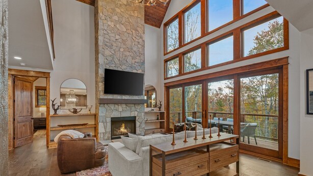 A spacious living room with a stone fireplace, a large TV, and a view of the outdoors through large windows.