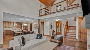 A spacious living area with a high ceiling, a dining area, and a staircase leading to an upper level.