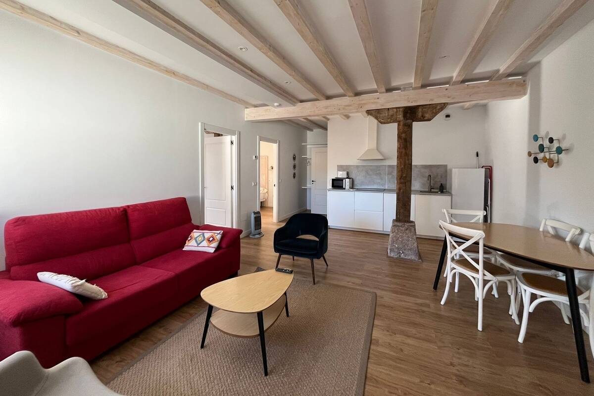Ein modernes Wohnzimmer mit einem roten Sofa, einem kleinen Couchtisch und einem Essbereich mit weißen Stühlen und einem Holztisch.