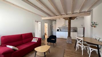 Een moderne woonkamer met een rode bank, een klein bijzettafeltje en een eethoek met witte stoelen en een houten tafel.