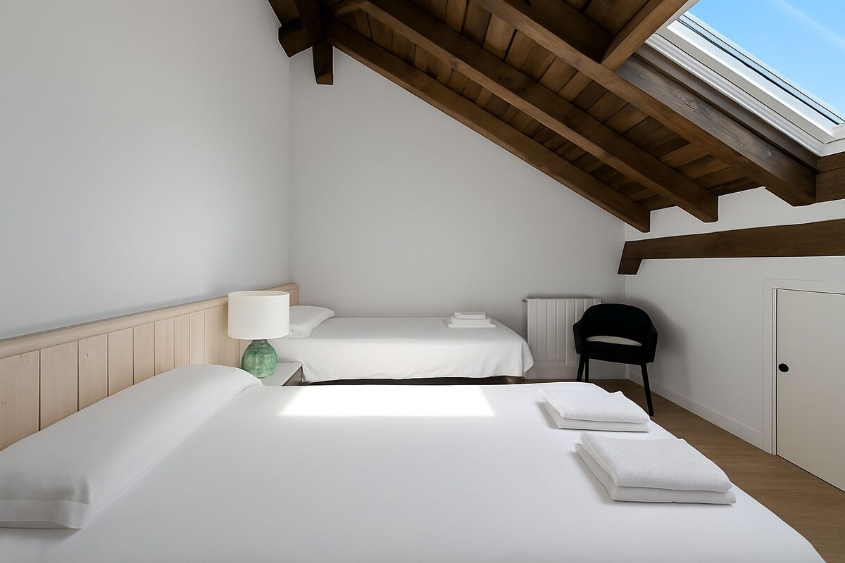 A bedroom with two beds, a chair, a lamp, and a skylight.