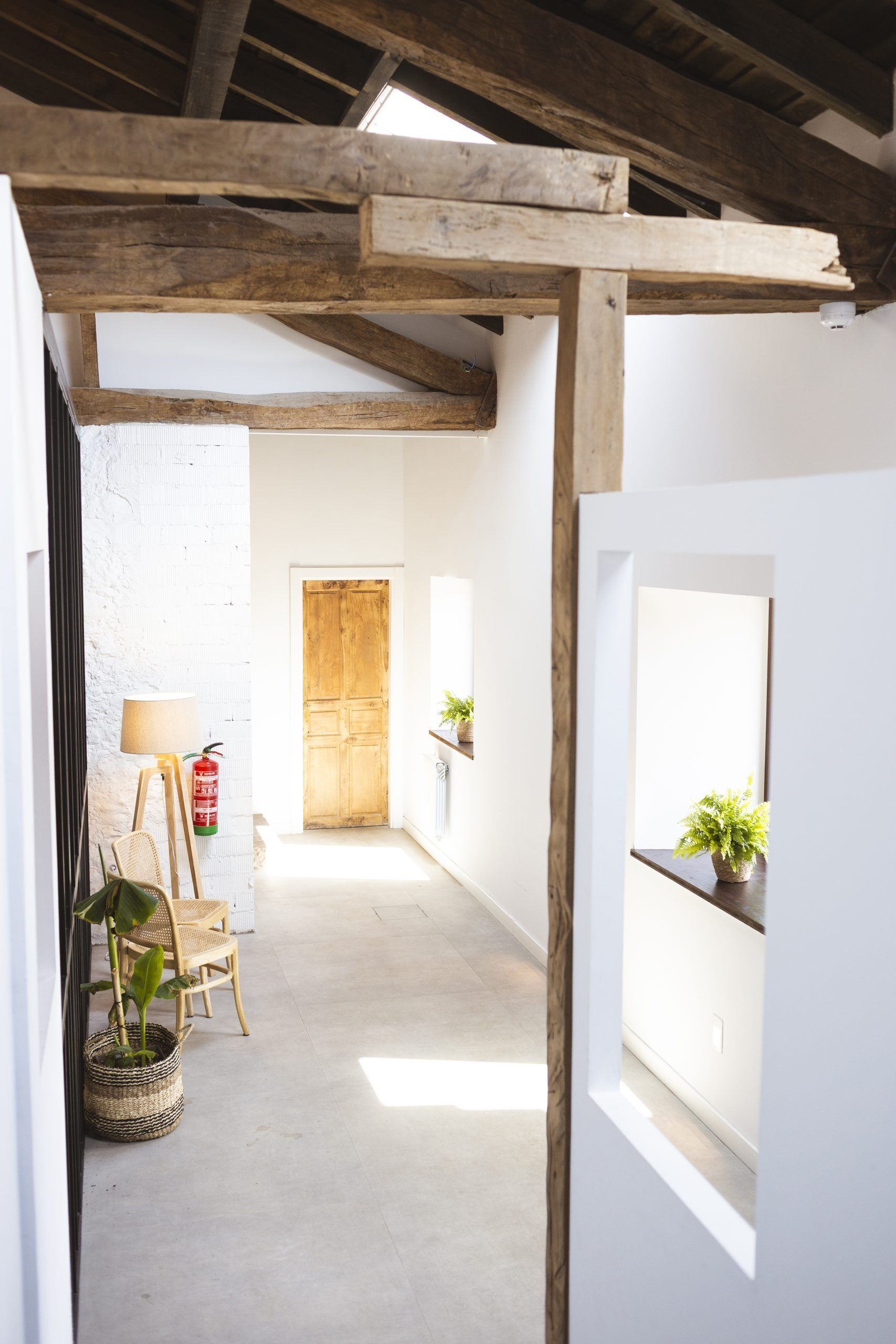 A narrow hallway with a wooden ceiling structure, a white door at the end, and a small table with a plant.