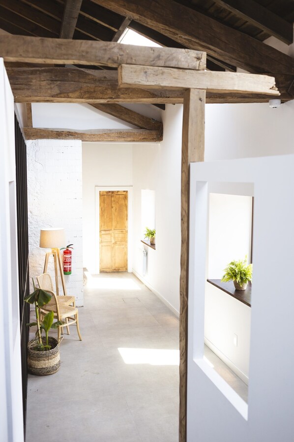 A narrow hallway with a wooden ceiling structure, a white door at the end, and a small table with a plant. - Otero de Campoo (Hermandad de Campoo de Suso)