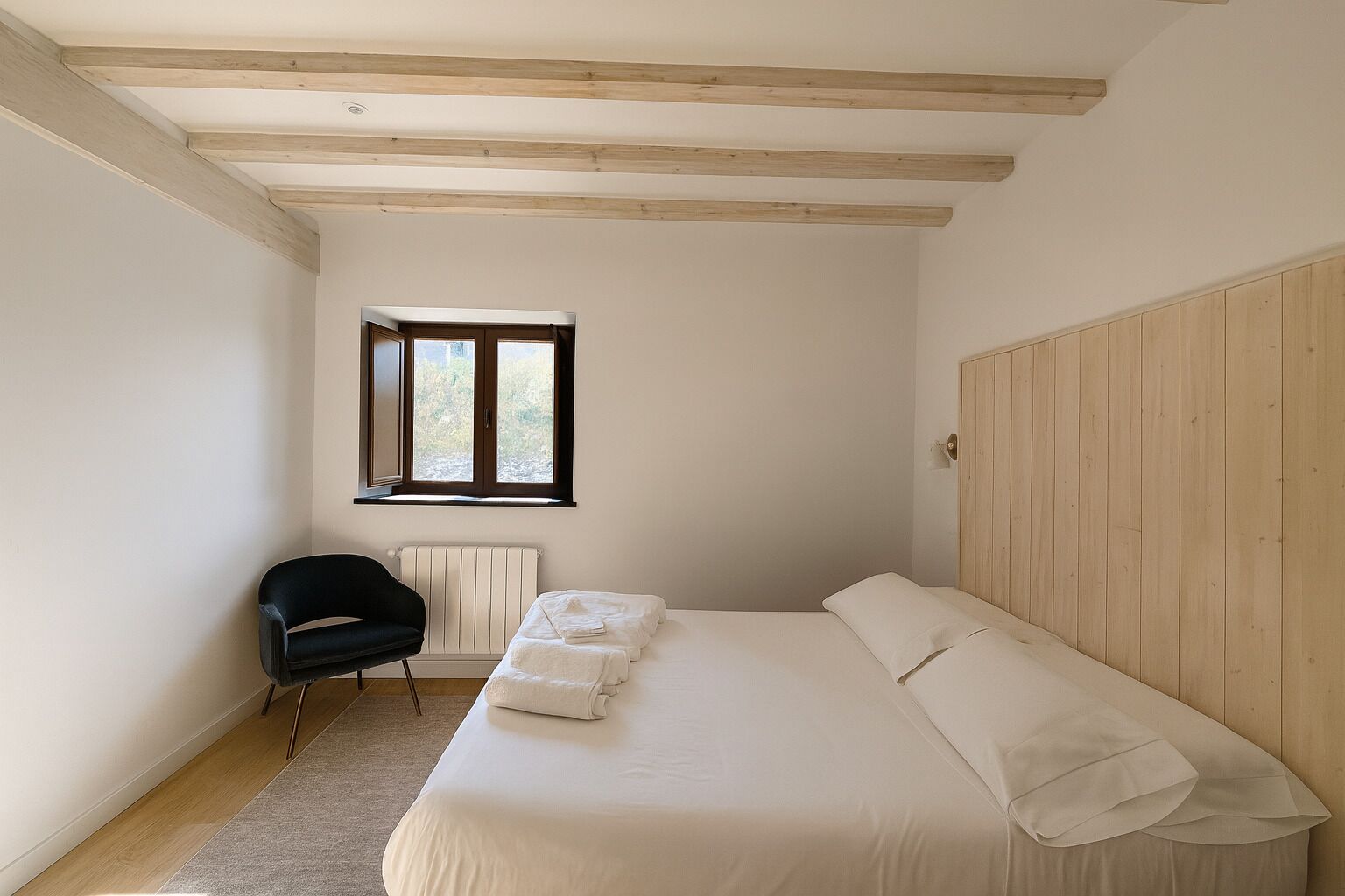 Een slaapkamer met een bed, een stoel, een raam en houten balken in het plafond.