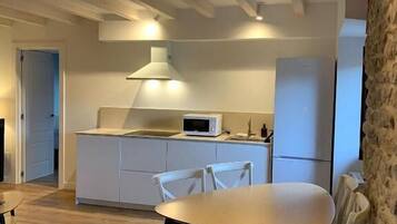 A modern kitchen with white cabinets, a microwave, and a built-in oven. There is a dining area with a wooden table and white chairs.