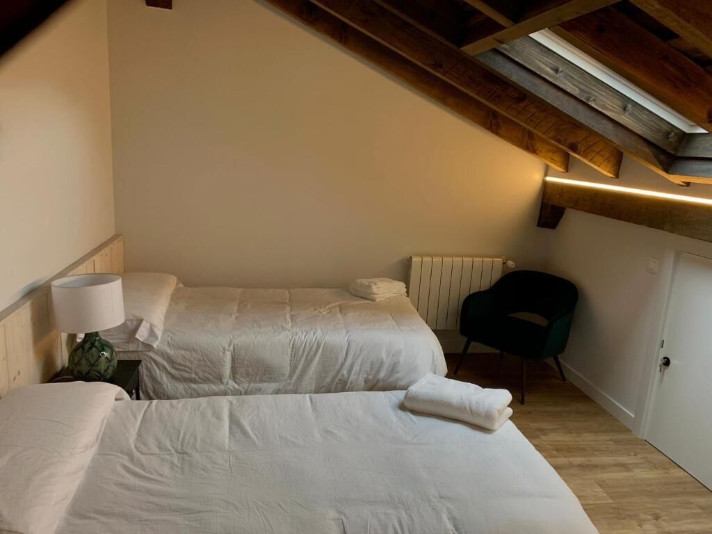 Quarto com duas camas, uma cadeira, um abajur e um radiador.