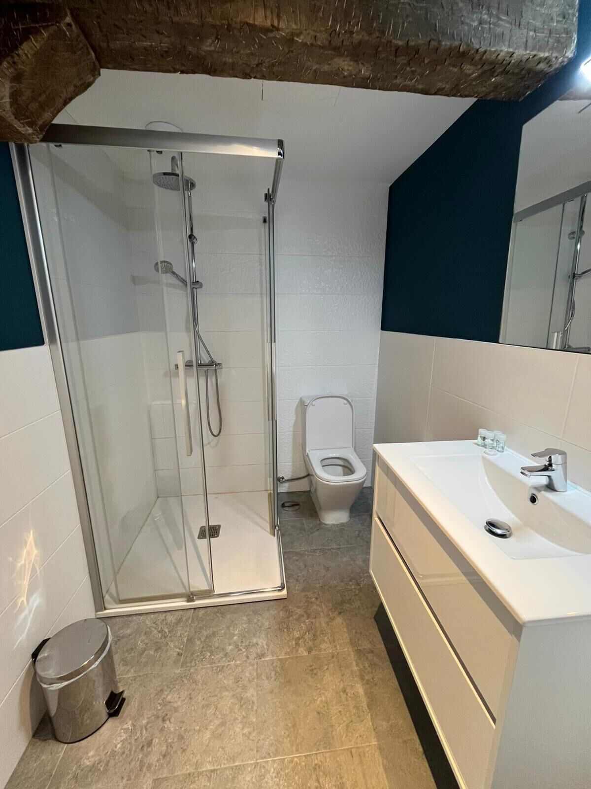 Un baño con ducha compartimentada con vidrio, un inodoro y un lavamanos blanco con espejo.