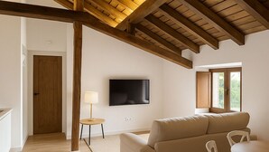 A modern living room with a wooden ceiling, a beige sofa, a TV mounted on the wall, and a window with a view. - Otero de Campoo (Hermandad de Campoo de Suso)