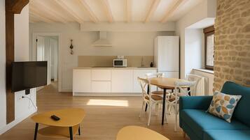 Una sala de estar moderna con un sofá, una mesa de centro y un televisor. Cuenta con una zona de cocina con una mesa de comedor y sillas.