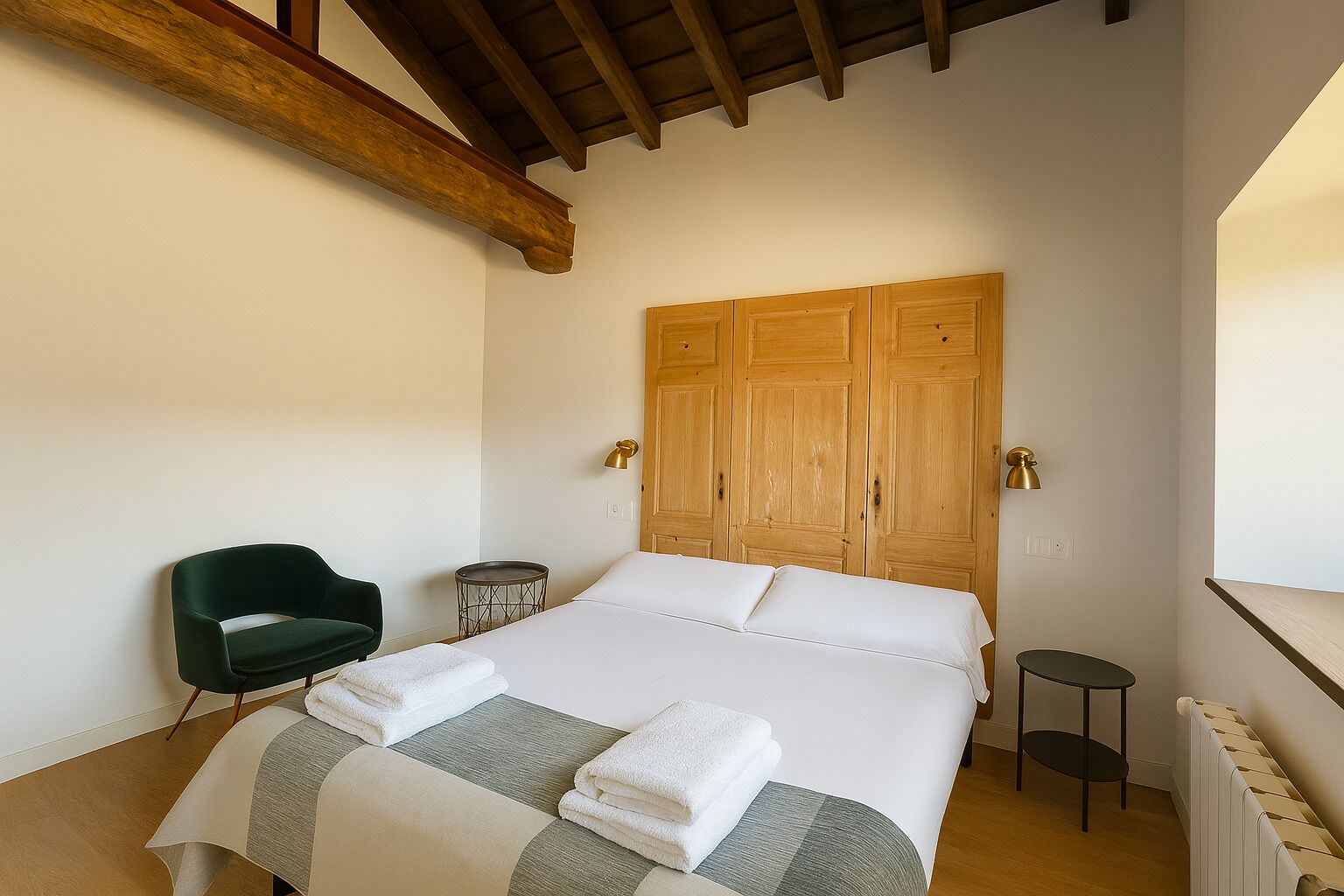 A bedroom with a bed, a green chair, a small round table, and wooden wardrobes.