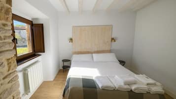 Una camera da letto con una testiera in legno, un letto con lenzuola bianche, un comodino e una finestra che si affaccia sul verde.