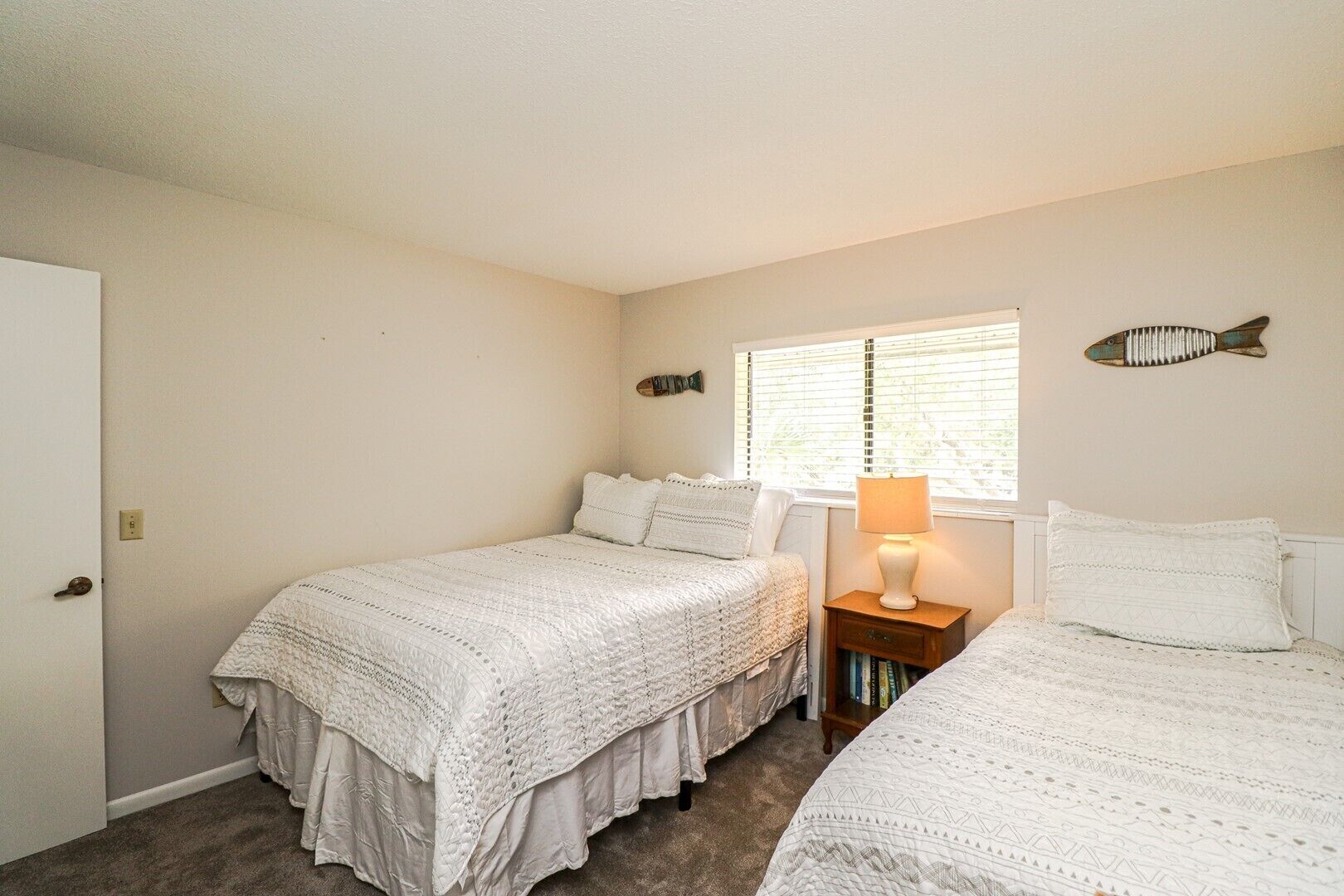A bedroom with two beds, a nightstand with a lamp, a window with blinds, and wall decorations.