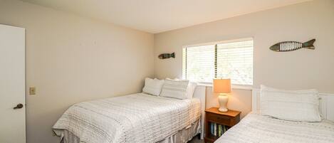 A bedroom with two beds, a nightstand with a lamp, a window with blinds, and wall decorations.