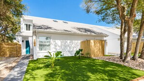 A modern house with a white exterior, a wooden fence, and a well-maintained lawn with a few plants.