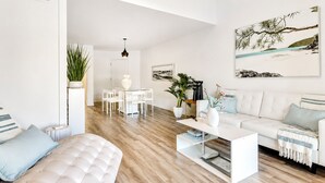 A modern living room with a white sofa, a coffee table, and a dining area with a white table and chairs. - Lux Beach Cabana - Close to Beach & Restaurants (St. Augustine)