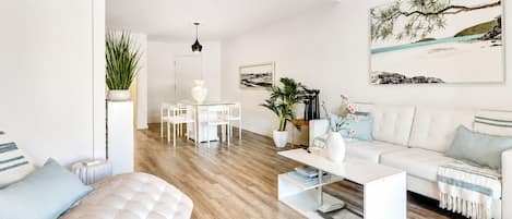 En moderne stue med en hvid sofa, et sofabord og et spiseområde med et hvidt bord og stole.