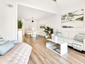 Un salon moderne avec un canapé blanc, une table basse et un coin repas comprenant une table et des chaises blanches.