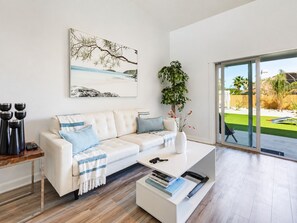 Een moderne woonkamer met een witte bank, een salontafel, een groot raam en een schilderij aan de muur.
