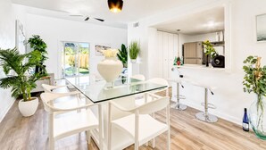 A modern kitchen with white cabinetry, a glass dining table, and a hanging pendant light. - Lux Beach Cabana - Close to Beach & Restaurants (St. Augustine)