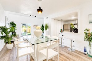 Une cuisine moderne avec des meubles blancs, une table à manger en verre et un luminaire suspendu.