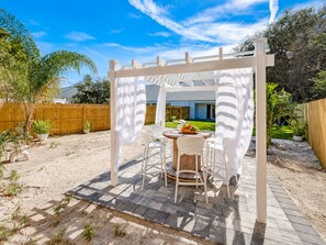 An outdoor patio with a white pergola, a round table, and chairs. - Lux Beach Cabana - Close to Beach & Restaurants (St. Augustine)