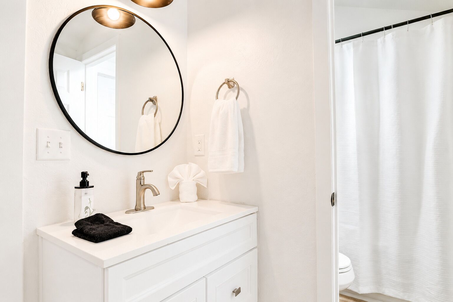 A bathroom with a white vanity, a round mirror, a towel rack, and a shower curtain.