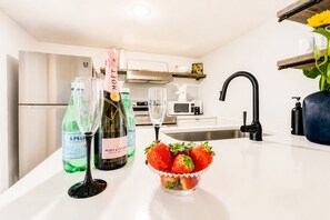 Una cocina moderna con encimera blanca, dos botellas de champán, un bol de fresas y un grifo negro.