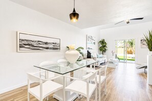 Een moderne eetruimte met een glazen tafel, witte stoelen en een witte vaas met bloemen.
