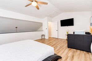 Un dormitorio moderno con una cama grande, un sofá negro, un televisor de pantalla plana y un ventilador de techo.