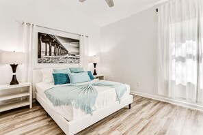 Une chambre à coucher avec un lit, des tables de chevet, une lampe, un tableau et une fenêtre avec des rideaux.