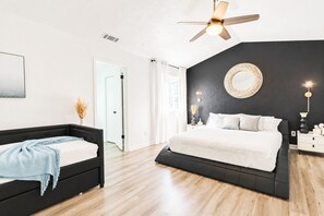 Een slaapkamer met een bed, nachtkastje, plafondventilator en een deur.
