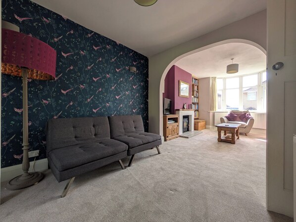Ein Wohnzimmer mit dunkler Wandmusterung, einem grauen Sofa, einem Holzschrank und einem Fenster mit Blick.