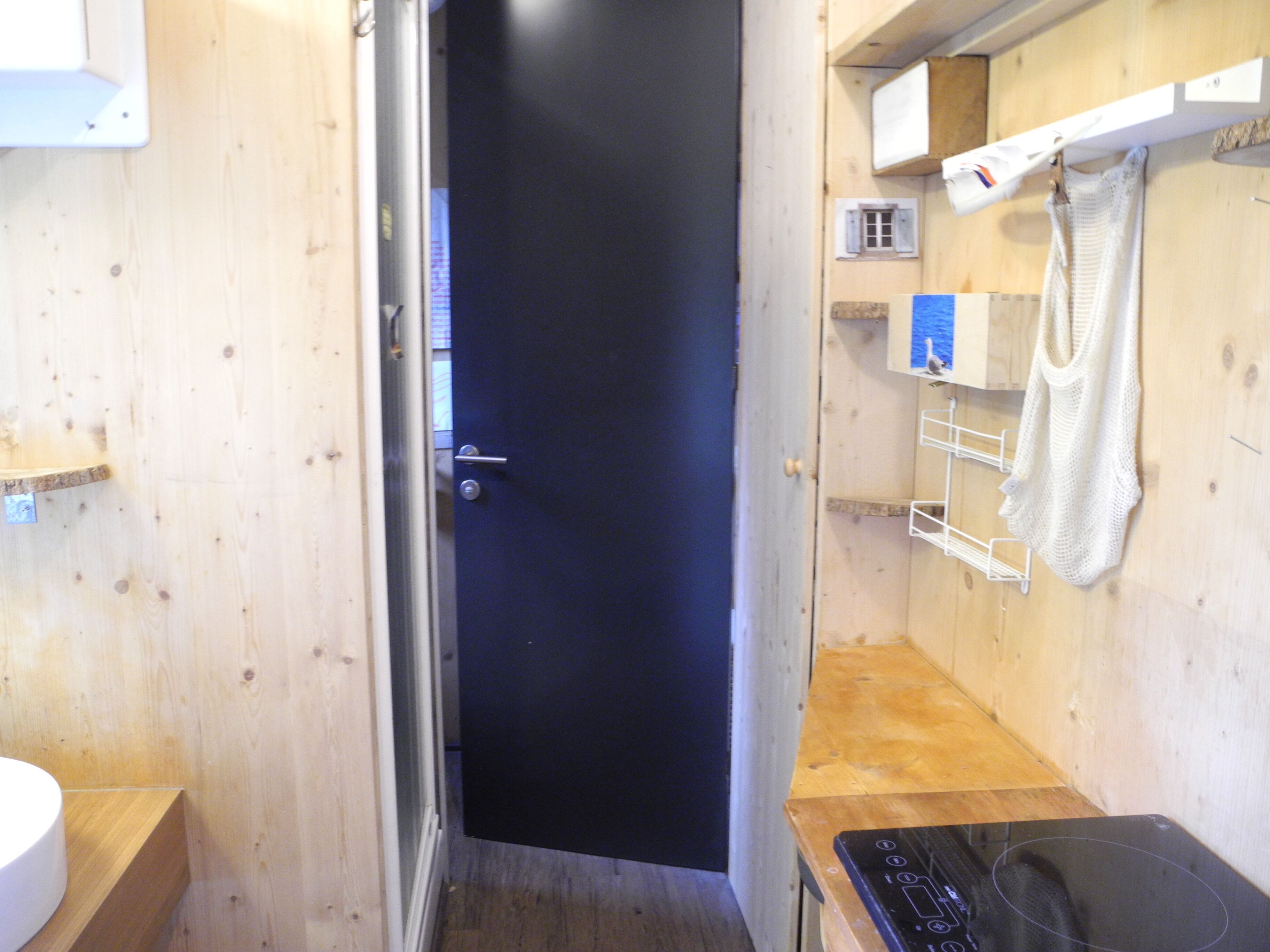 Baño pequeño y funcional con detalles de madera, una puerta negra, un lavamanos blanco y un perchero.